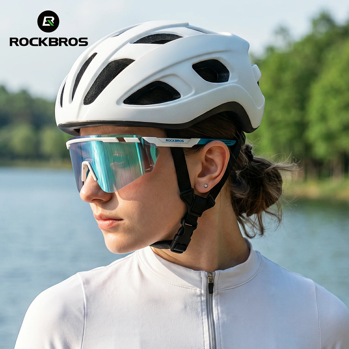 A woman in a white cycling jersey wearing a white Rockbros cycling helmet and mirrored shield glasses, photographed outdoors with water and trees in the background. #Color_Blue