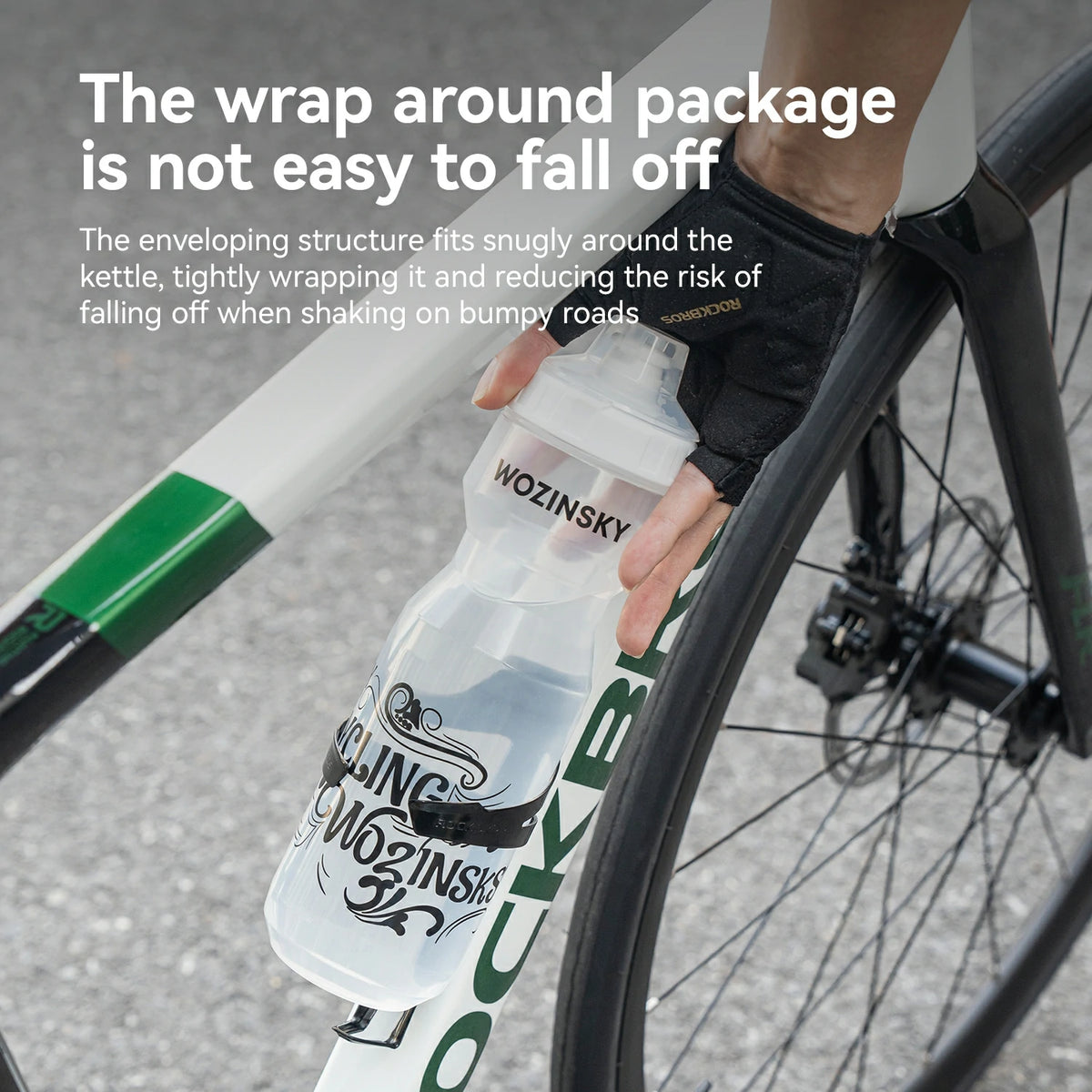 A close-up of a person's hand wearing a black cycling glove and holding a clear Wozinsky cycling bottle with a black and white label, wrapped around a road bike frame and wheel. White text at the top explains the bottle's secure wrap design.