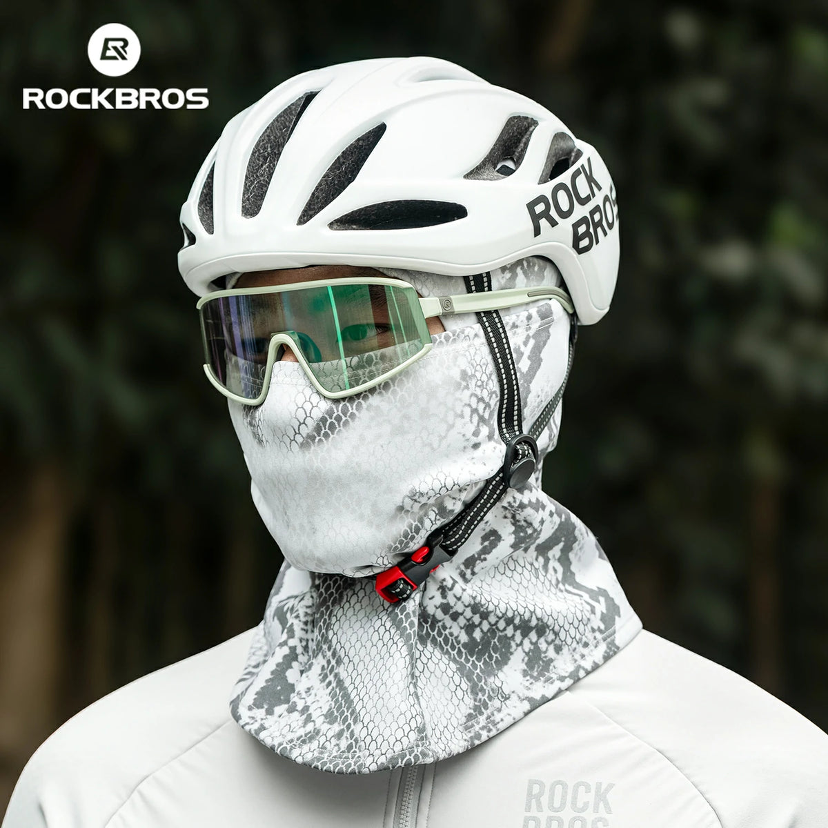 Person wearing a white helmet and face mask with 'RockBros' branding, against a blurred natural background. #color_Serpentine gray