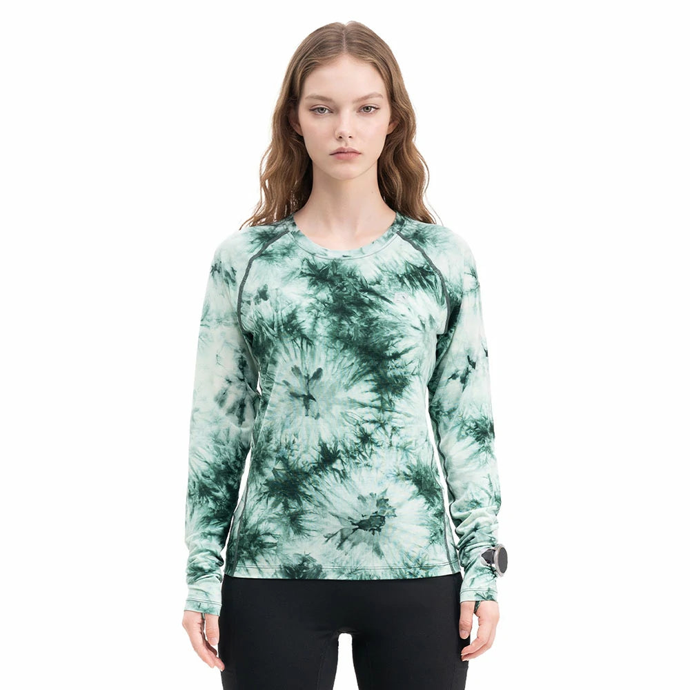 A woman modeling a long-sleeve crewneck athletic top with a green and white tie-dye pattern, paired with black leggings, against a plain white background.