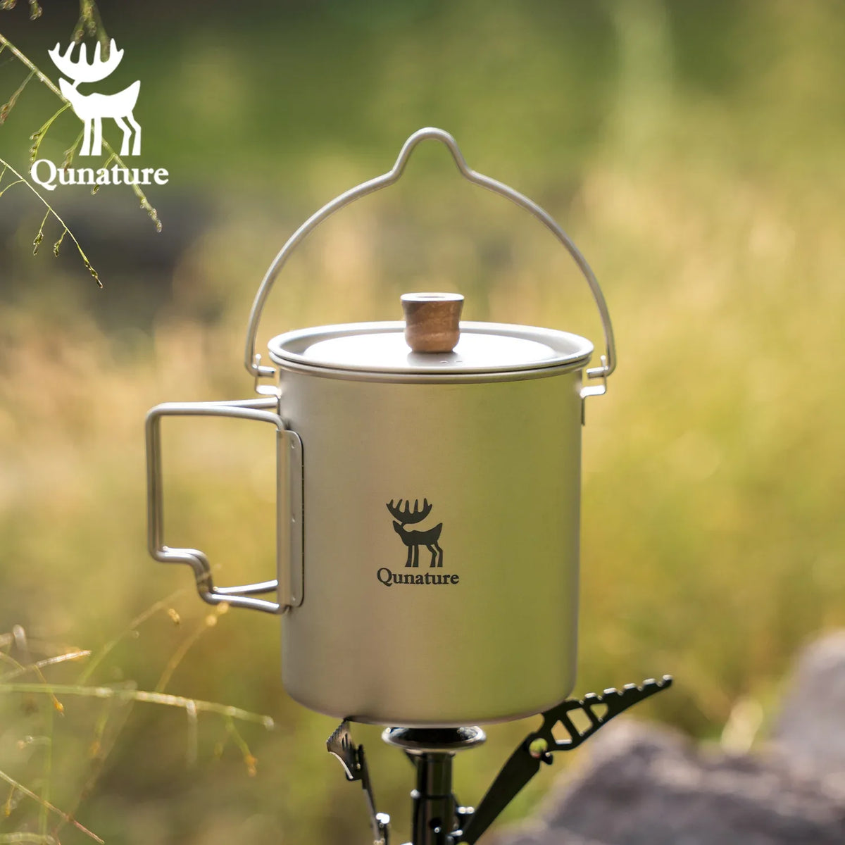 Camping mug with handle on a stand against a natural background, featuring Qunature logo.