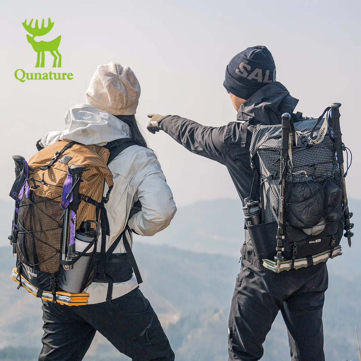 A girl with a khaki waterproof backpack and a boy with a black waterproof backpack on the top of a mountain