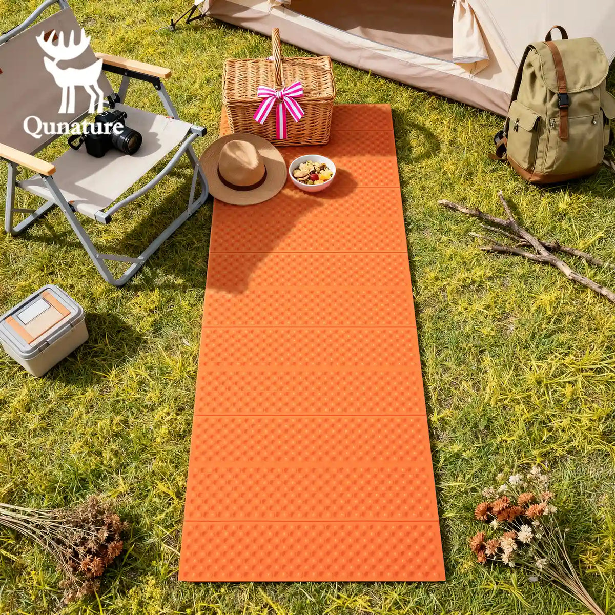 Orange camping mat on grass with outdoor furniture and items, featuring Qunature logo.