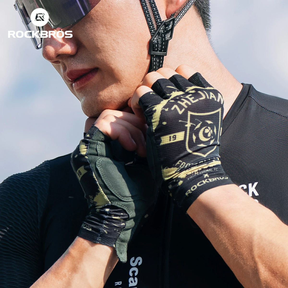 Person wearing black and green gloves with 'RockBros' branding against a clear sky.