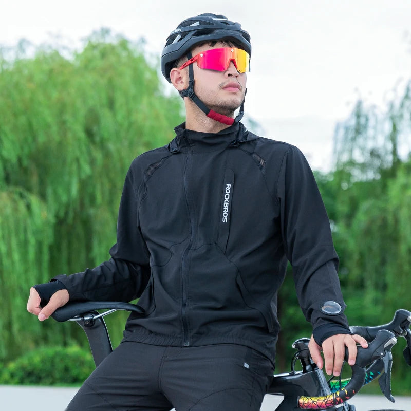 Person wearing a black cycling outfit with a helmet and sunglasses, sitting on a bicycle outdoors.