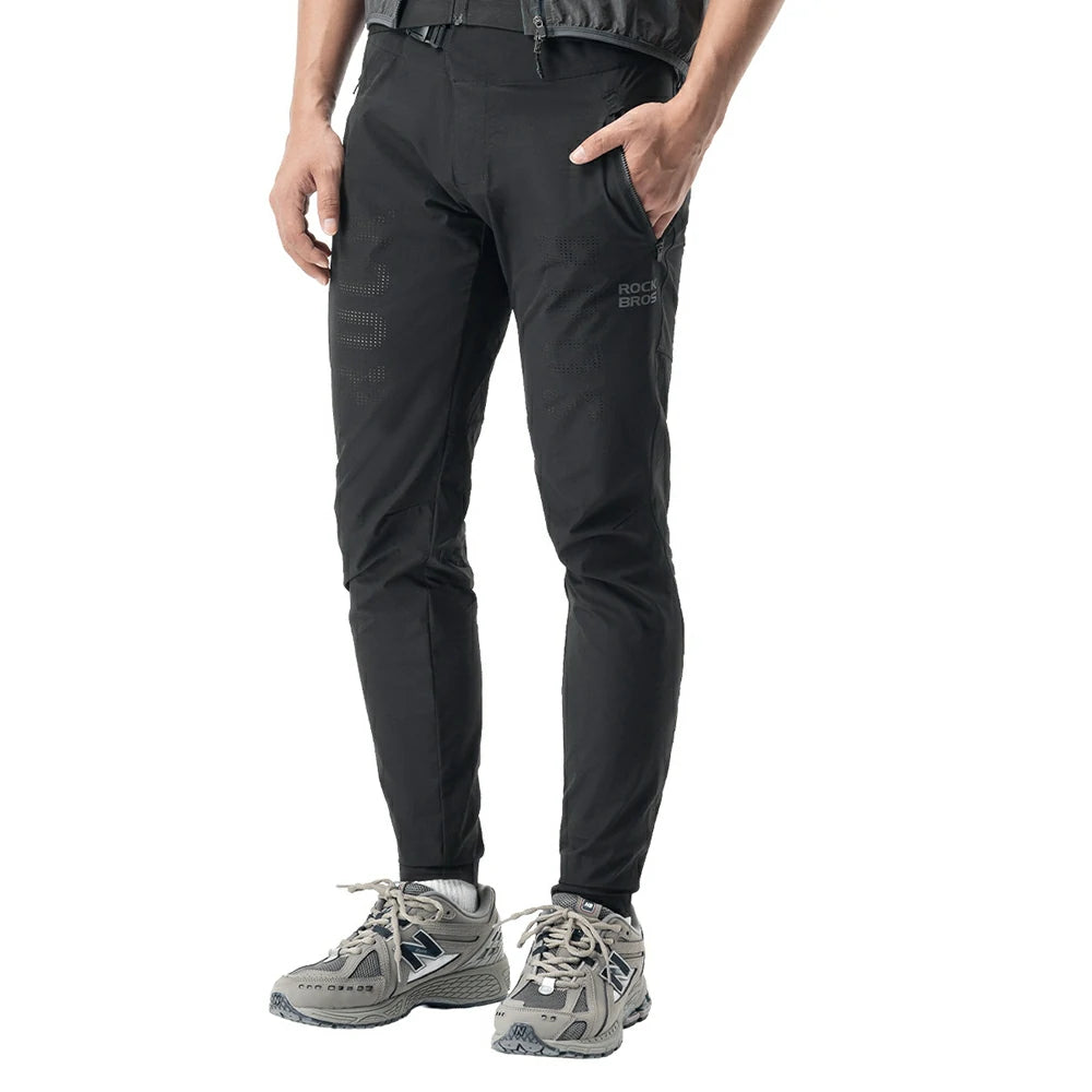 A person wearing black pants with gray trail running shoes, shown from the waist down against a plain white background.