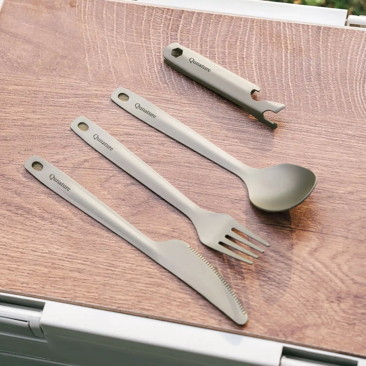 Set of stainless steel utensils including a fork, knife, spoon, and bottle opener on a wooden surface.