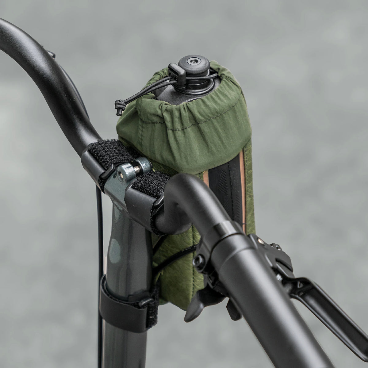 Green bag attached to a bicycle handlebar with a blurred gray background
